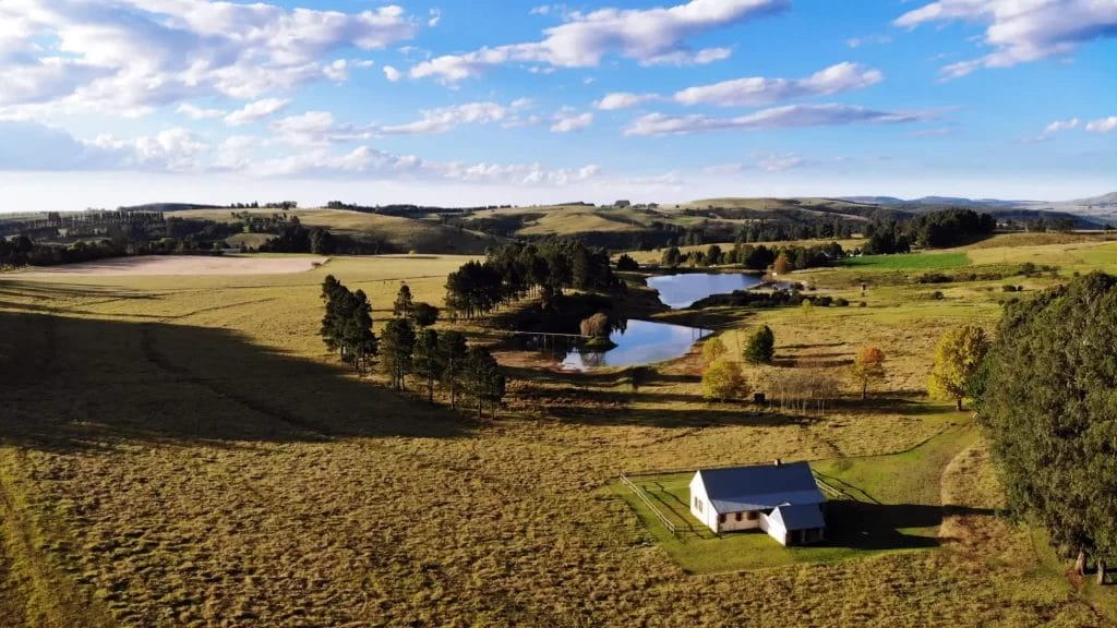 Aerial view of a rural landscape with rolling hills, a body of water, and a solitary building.
