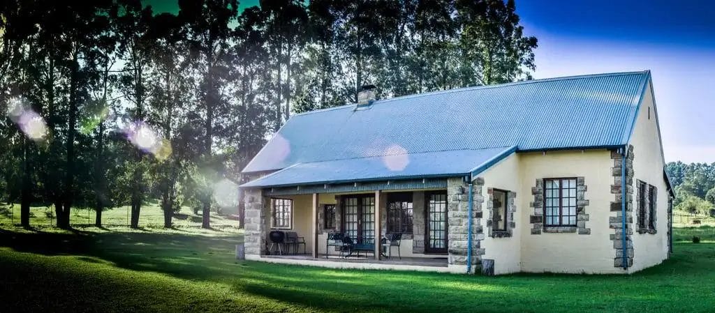 Country house with stone accents surrounded by greenery under a clear sky at dusk with lens flare effects.