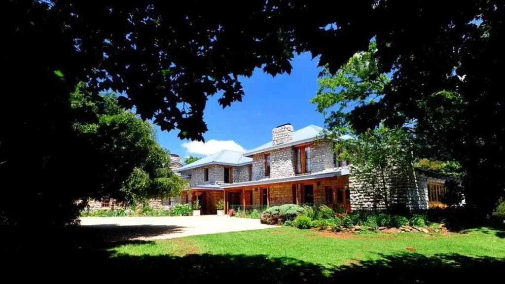 A traditional stone house framed by leafy tree branches under a clear blue sky.