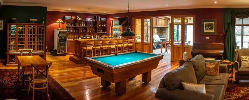Panoramic view of a cozy home interior with a billiards table, bar area, and seating space with bookshelves.