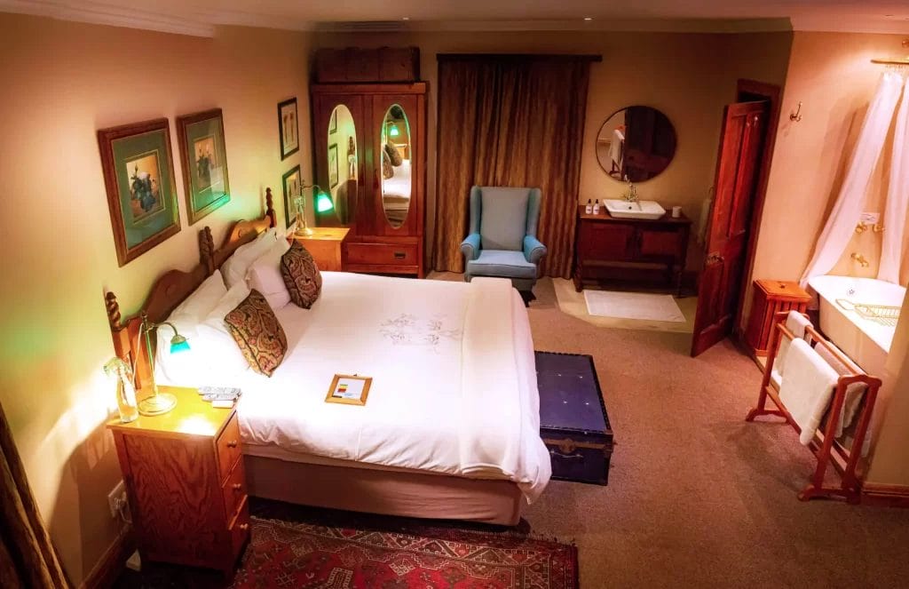 A warm and inviting hotel room interior featuring a large bed, seating area, and an adjoining open bathroom.