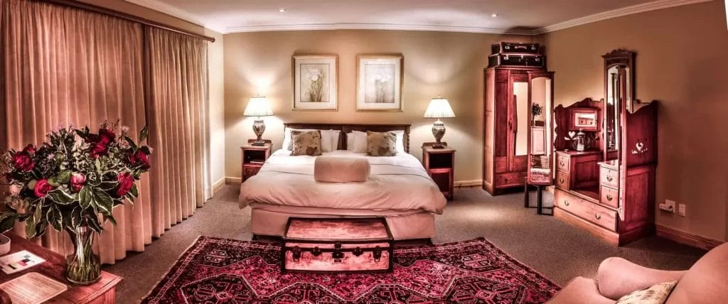 Elegantly furnished bedroom with a king-sized bed, traditional wooden furniture, and a decorative red rug.