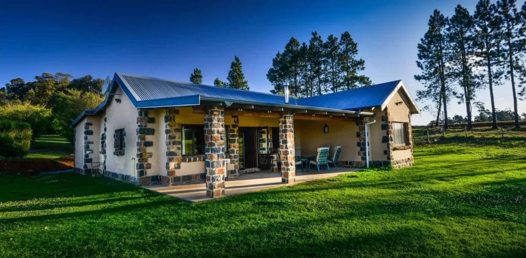 Stone cottage with a blue roof surrounded by lush greenery under clear skies.