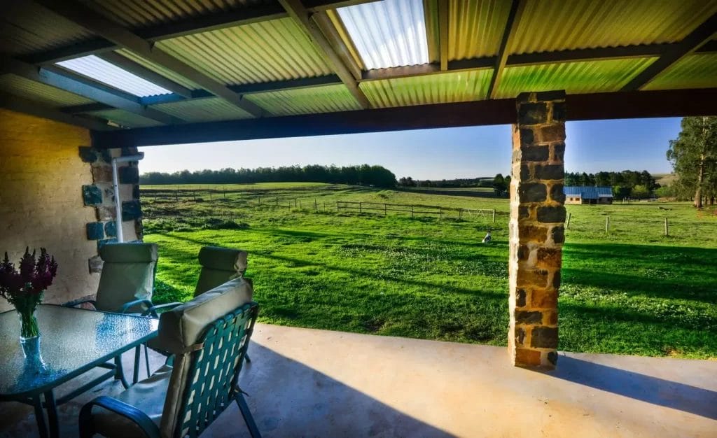 A rustic patio area opening onto a tranquil grassy field with a clear sky overhead.